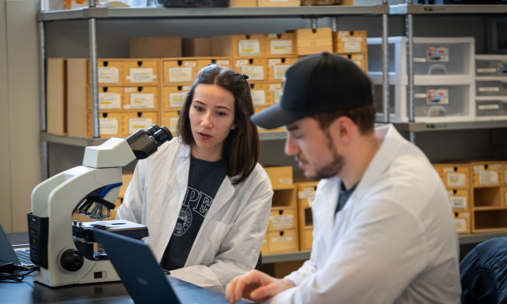 Alissa Kich looks on as a fellow student types on a laptop.