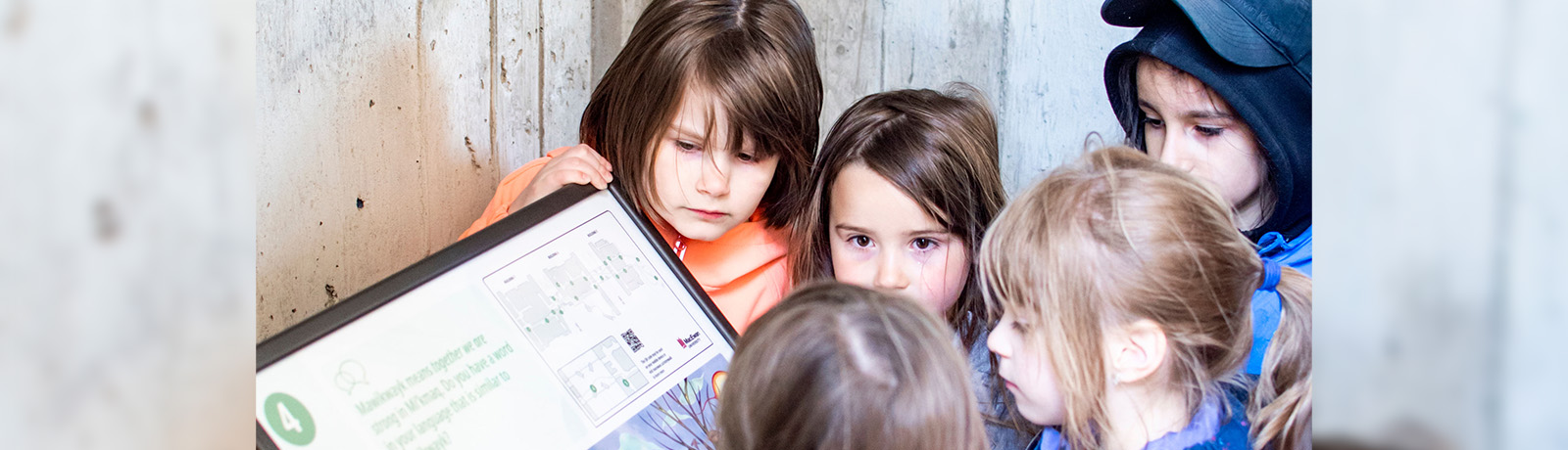 Children crowd around a sign with a page from a StoryWalk book