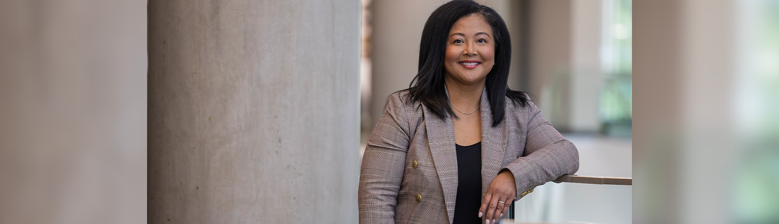 Rhodora leans against a railing in Allard Hall, wearing a tweed blazer.