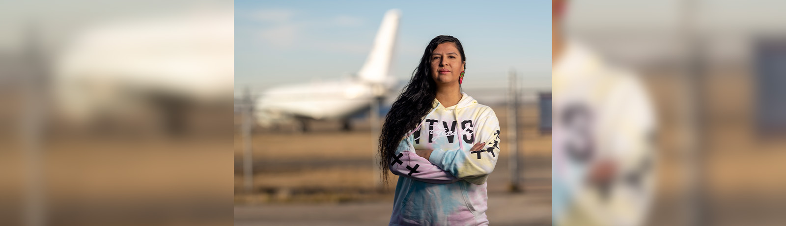 Mallory Yawnghwe stands with her arms folded across her chest, with a plane in the background.