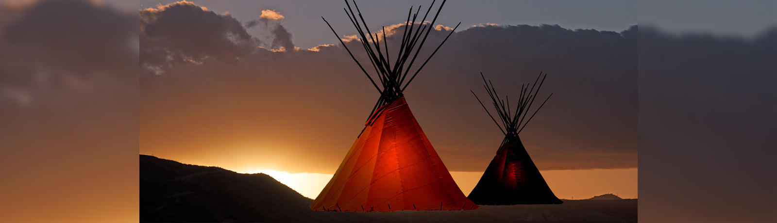 Two tipis backlit against a sunset