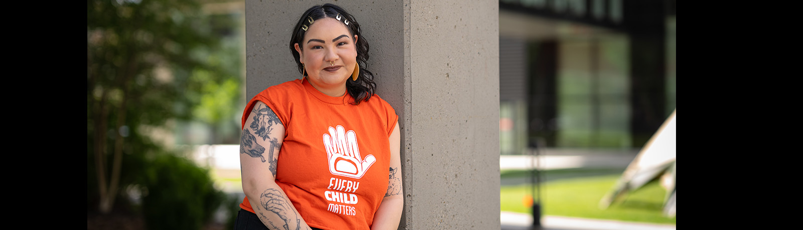 Caitlin Semaganis stands outside the kihew waciston Indigenous Centre wearing an \\"Every Child Matters\\" orange shirt