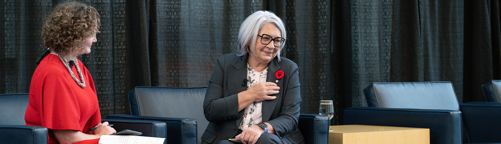 Mary Simon wears a grey blazer and sits on a chair opposite Sheena Rossiter.