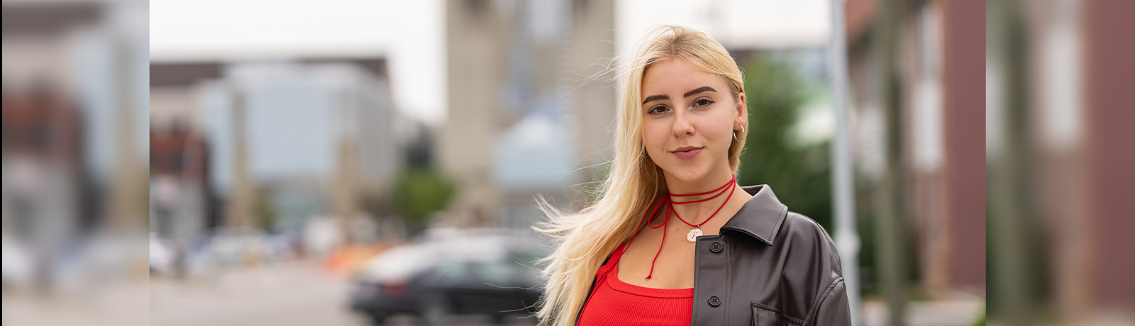 Sofia Budianska stands outside behind MacEwan's campus with the towers in the background