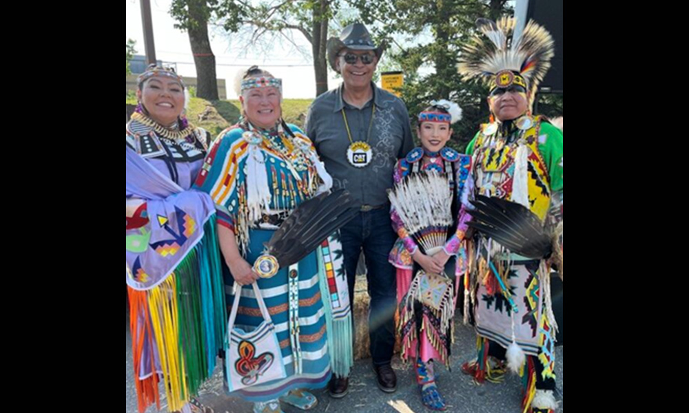 A group of people stand together in traditional Indigenous ceremonial attire.