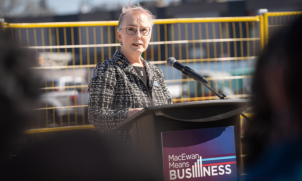 Carolyn Graham stands at a podium and speaks at the MacEwan School of Business Building groundbreaking.