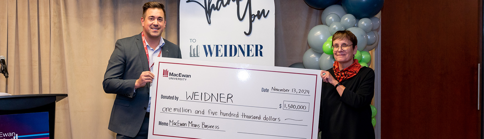 Two people stand in front of a sign and hold opposite ends of a jumbo cheque.