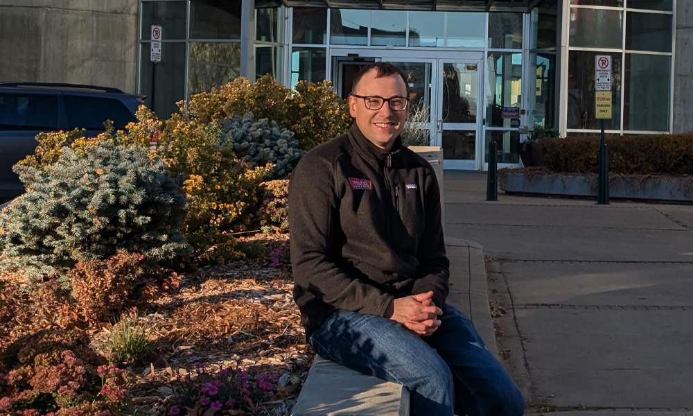 Neal Hamacher sits alongside a flower bed outside of MacEwan's clock tower entrance.