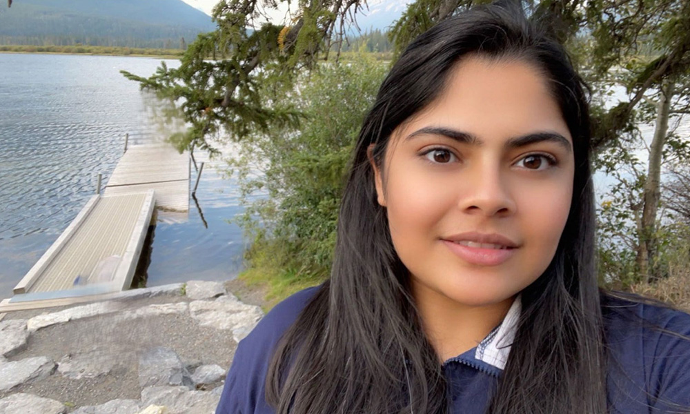 Deeksha Narula stands in front of a pier leading out onto a lake.