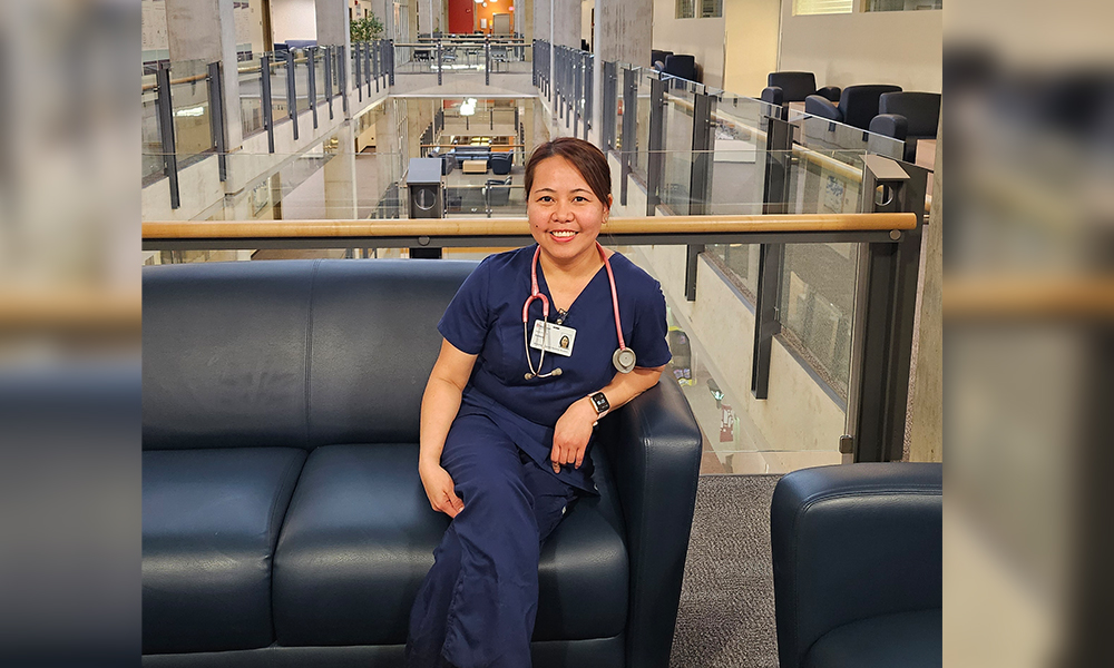 Vanessa Trasmonte sits on a couch in Building 9 wearing blue scrubs.