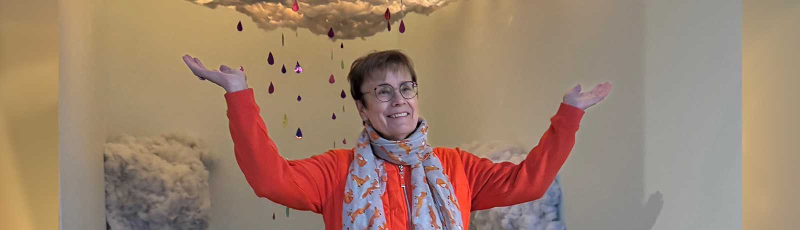 Dr. Trimbee with her arms outstretched stands under an art installation of a raincloud