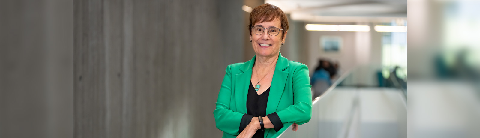 Dr. Trimbee wears a green blazer and leans on a glass railing in Allard Hall.