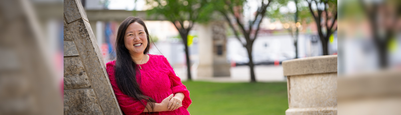 Dr. Lipes wears a red dress and leans against a concrete wall outside of Building 6.