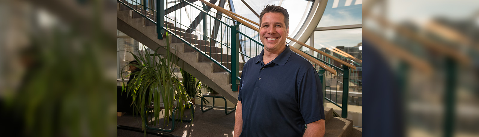 A man smiles at the camera, standing in front of a staircase