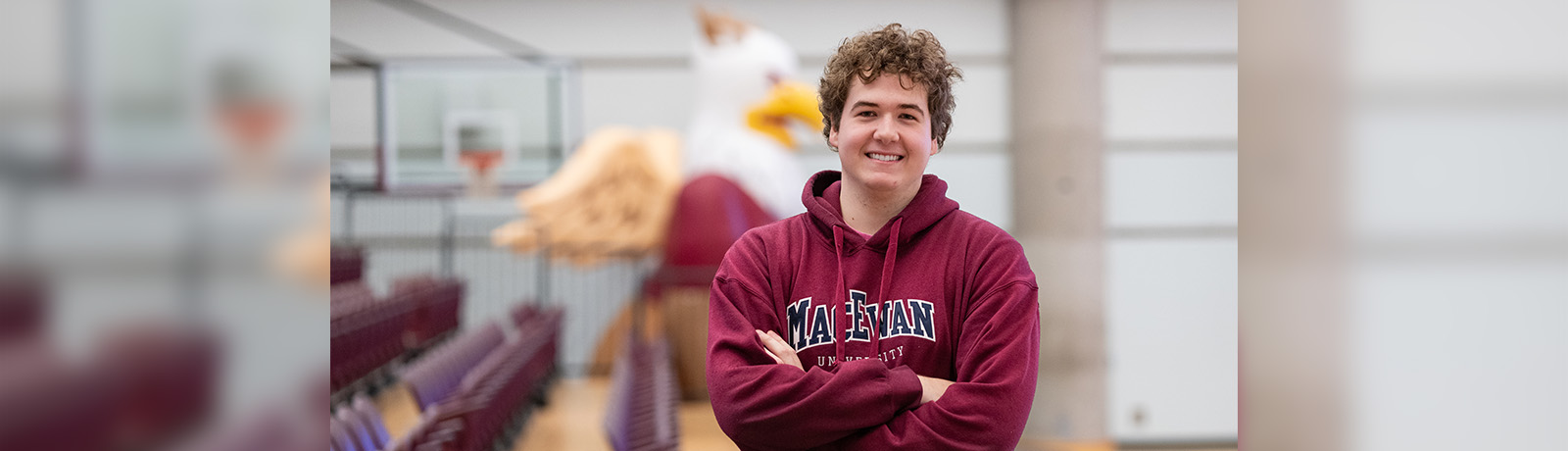 A student standing, arms crossed and smiling, in front of rows of bleachers