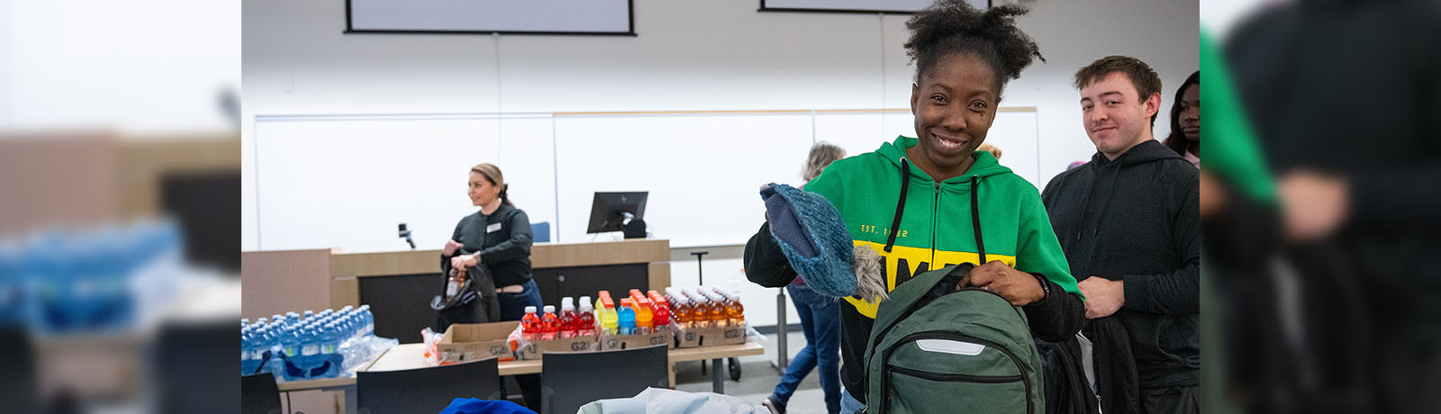 Ronique Holgate places a green toque in a backpack. Bottles of water and energy drinks are in the background, along with other people helping to fill backpacks