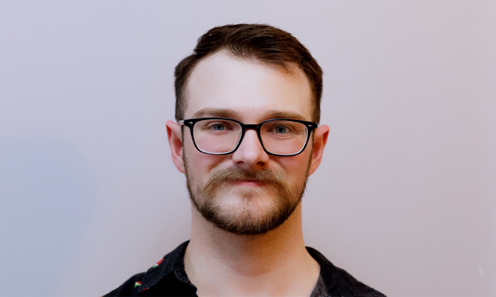 A headshot of Joel Roy over a grey background.