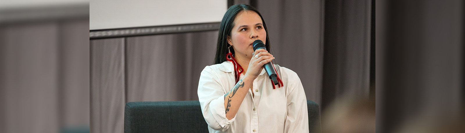 Sydney Frances Pascal wears long red earrings and speaks into a microphone at the opening of her gallery.