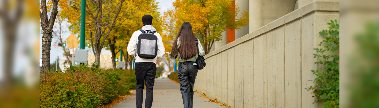 Two students are seen from behind walking toward campus, wearing backpacks.