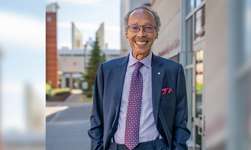 Dr. Fields stands outside of Building 9 on campus wearing a navy blue suit.